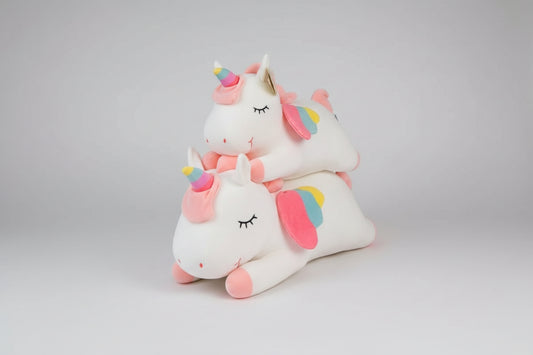 White unicorn plush toys with rainbow horns and pastel wings stacked on a light grey background.