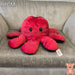 90cm reversible octopus plush toy with happy red face and black reverse side displayed on a grey armchair.
