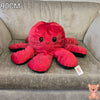 90cm reversible octopus plush toy with happy red face and black reverse side displayed on a grey armchair.