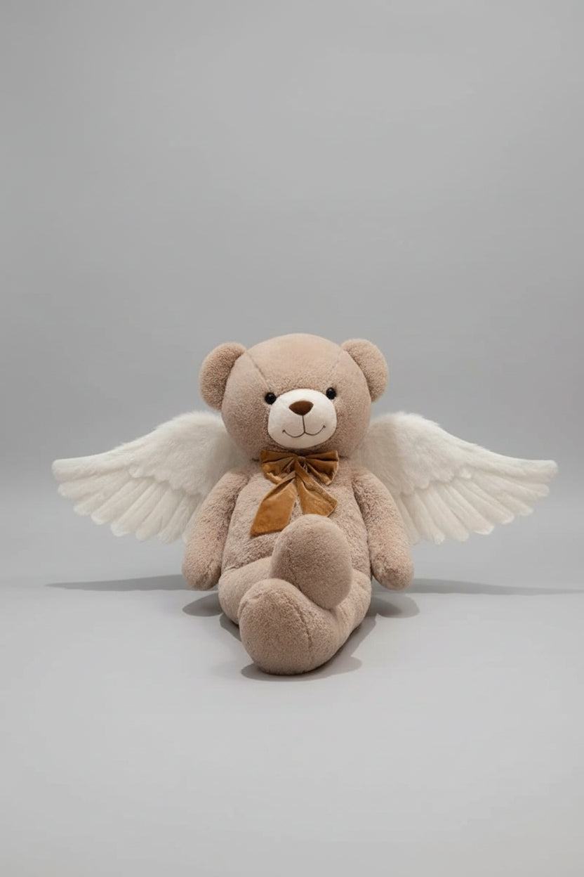 Angel teddy bear plush toy with white wings and brown ribbon bow sitting on a light grey background