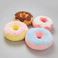 Collection of donut plush pillows featuring chocolate, pink, blue and vanilla frosting designs with colourful sprinkles.