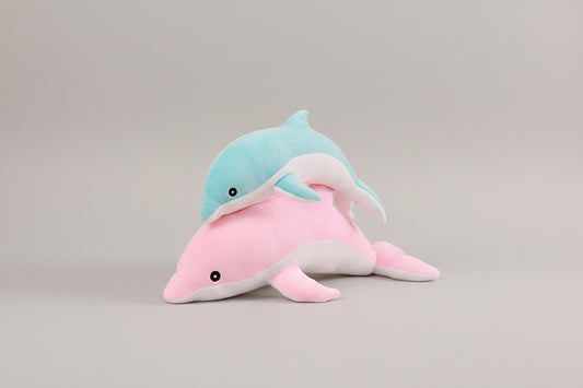Blue dolphin plush toy resting on a pink dolphin plush toy on a light neutral background