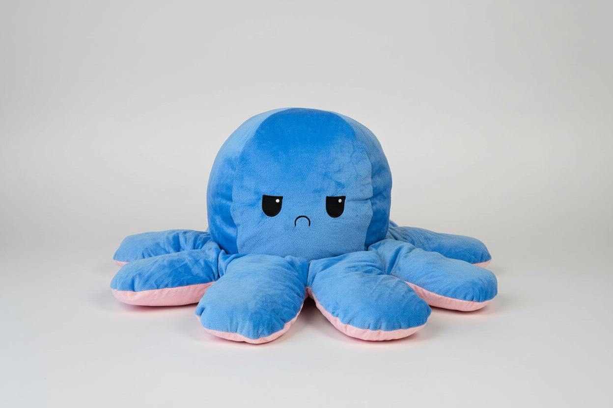 Blue and pink reversible octopus plush toy with sad face on a white background.