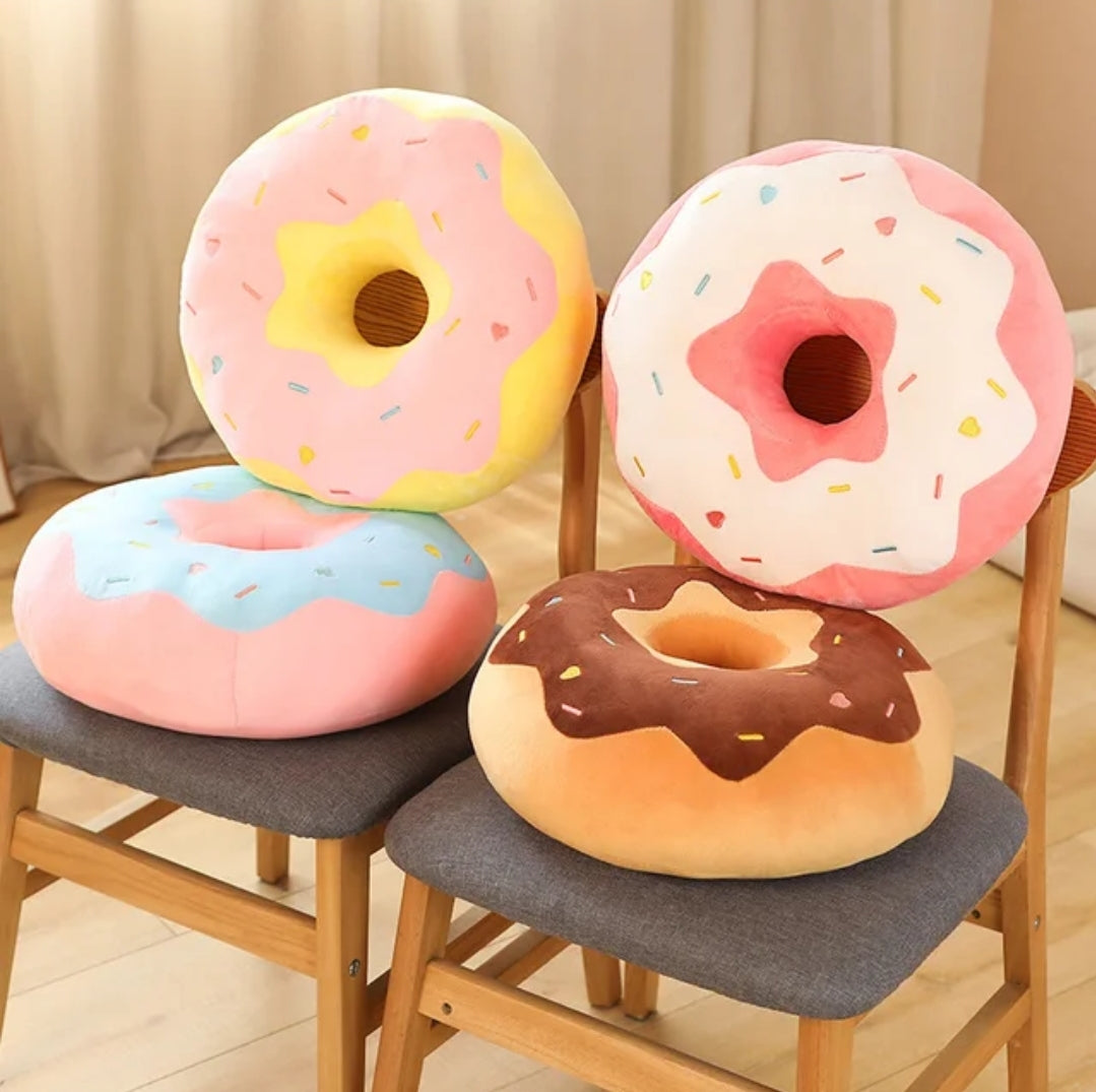 Assorted donut plush pillows in pink, blue and chocolate frosting designs displayed on wooden chairs.