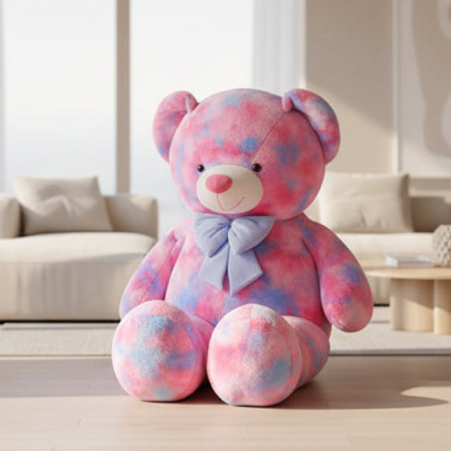 Large pastel teddy bear plush toy in pink and blue colours with a bow sitting in a modern living room