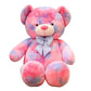 Large pastel teddy bear plush toy in pink and purple colours with a decorative bow displayed on a white background
