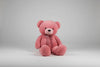 Large pink teddy bear plush toy with a satin bow sitting on a grey background