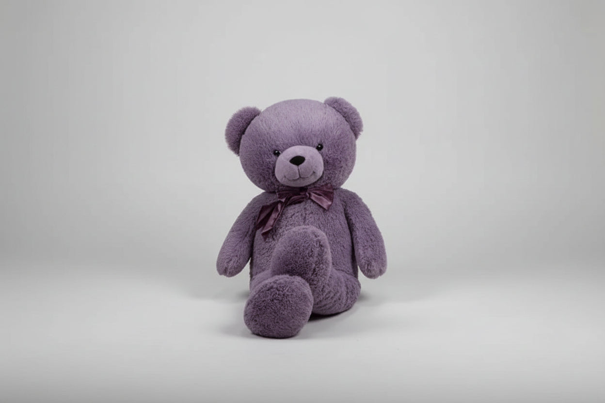 Large purple teddy bear plush toy with a satin bow sitting on a light grey background