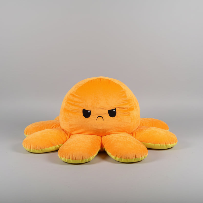 Orange and yellow reversible octopus plush toy with sad face on a light grey background.