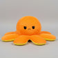 Orange and yellow reversible octopus plush toy with sad face on a light grey background.