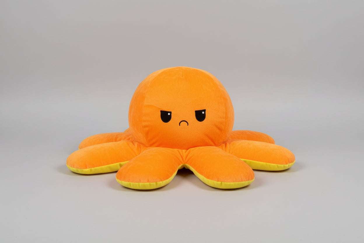 Orange and yellow reversible octopus plush toy with sad face on a light grey background.