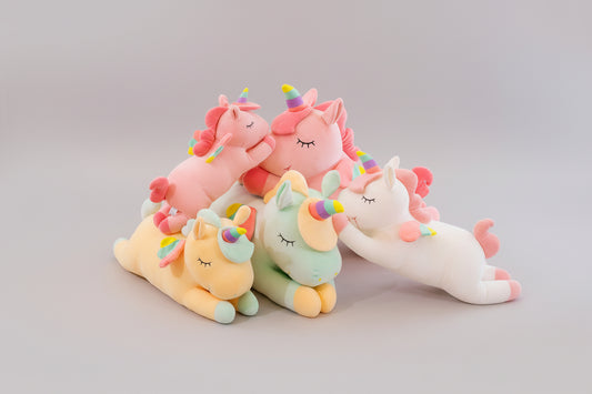 Pastel unicorn plush toy collection in pink, white, yellow and green colours on a light grey background.