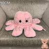 90cm pink and blue reversible octopus plush toy with happy face displayed on a grey armchair.