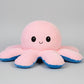 Pink and blue reversible octopus plush toy with happy face on a white background.