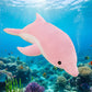 Pink dolphin plush toy swimming above a colourful coral reef with tropical fish in an underwater ocean scene.