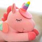 Close-up of a pink unicorn plush toy with rainbow horn and pastel wings resting on a sofa.