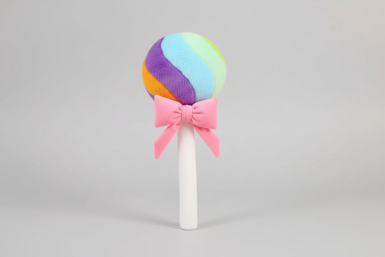 Rainbow lollipop plush toy with pink ribbon bow on a light grey background.