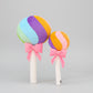 Rainbow lollipop plush toys with pink ribbon bows displayed on a light grey background.