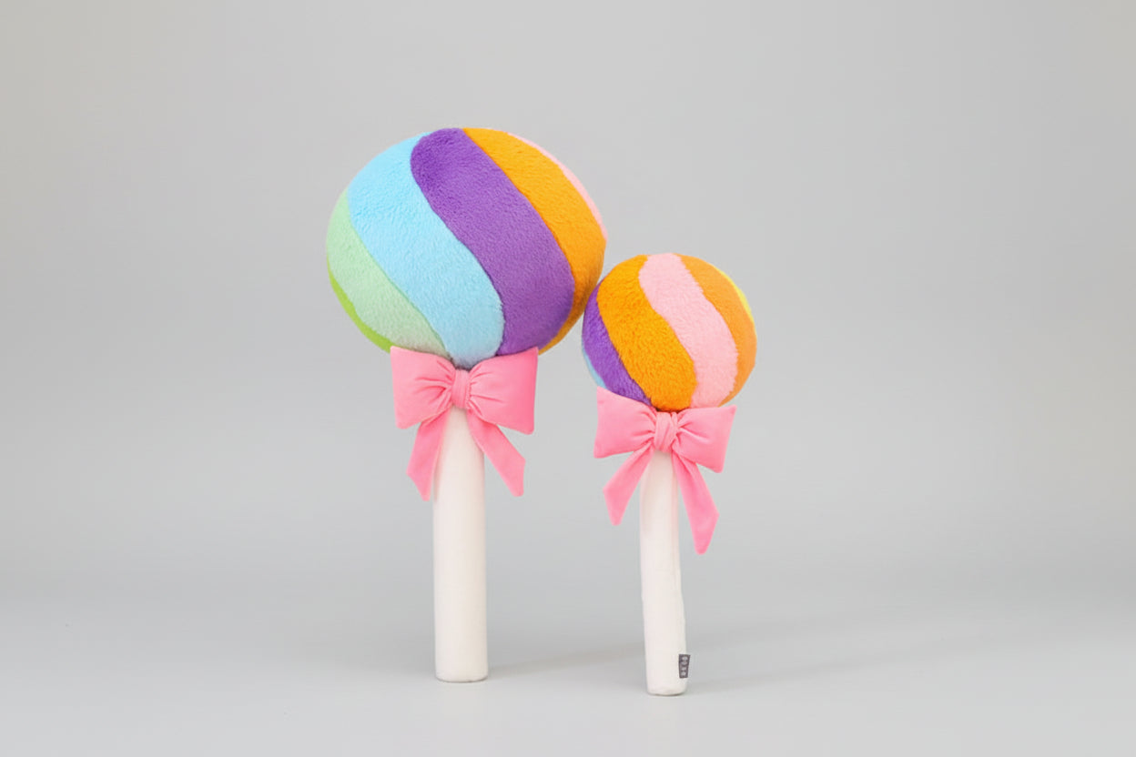 Rainbow lollipop plush toys with pink ribbon bows displayed on a light grey background.
