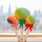 Rainbow lollipop plush toys with colourful bows displayed in front of a city skyline window view.
