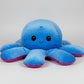 Close-up view of a reversible blue and purple octopus plush toy with happy expression on a white background.