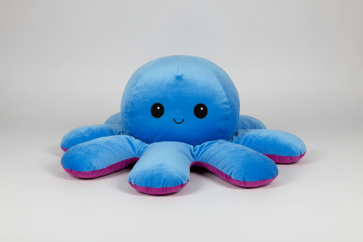 Close-up view of a reversible blue and purple octopus plush toy with happy expression on a white background.