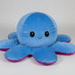Reversible blue and purple octopus plush toy with happy expression, soft stuffed cushion shown from the front on a white background.