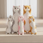Standing cat plush toy family collection in grey, pink and orange colours displayed together in a bright living room.