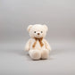 White teddy bear plush toy with a brown ribbon bow sitting on a light grey studio background