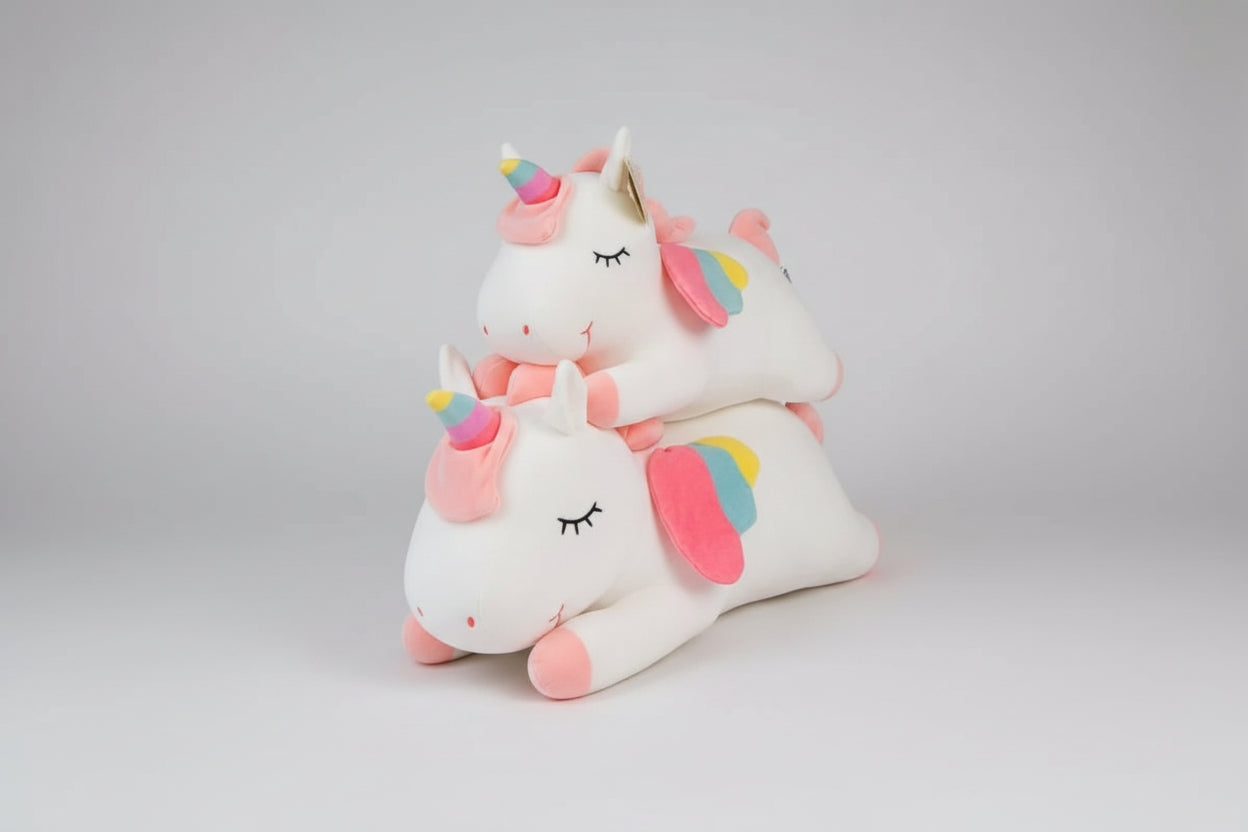 White unicorn plush toys with rainbow horns and pastel wings stacked on a light grey background.