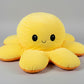 Yellow and orange reversible octopus plush toy with happy face on a light grey background.