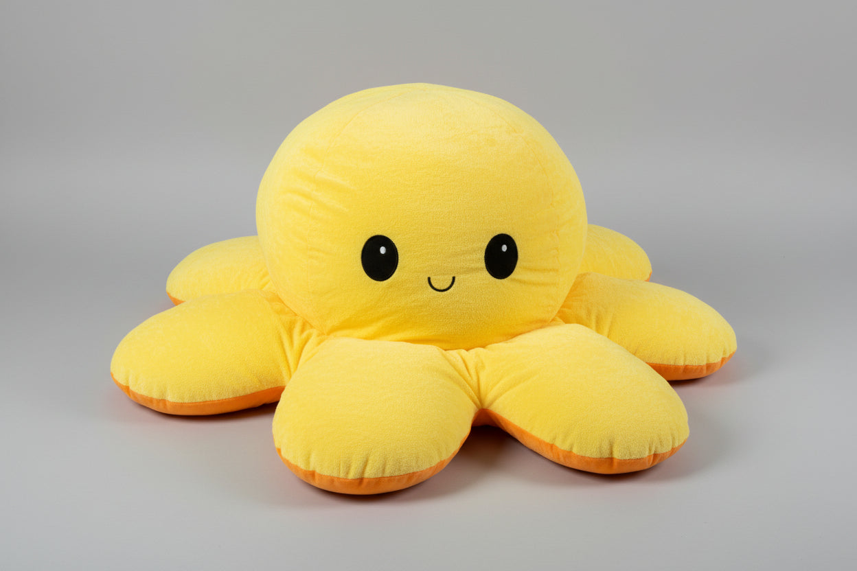 Yellow and orange reversible octopus plush toy with happy face on a light grey background.