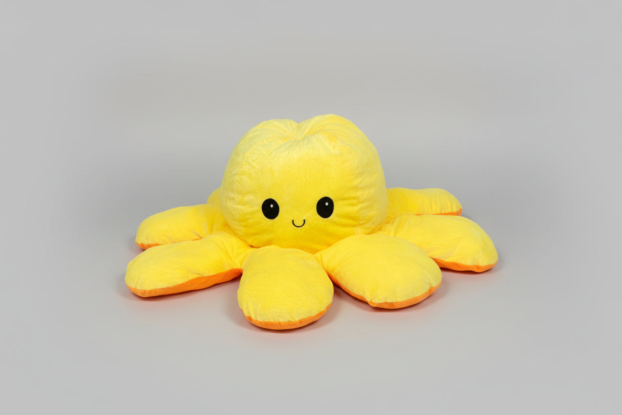 Yellow and orange reversible octopus plush toy with happy face on a light grey background.