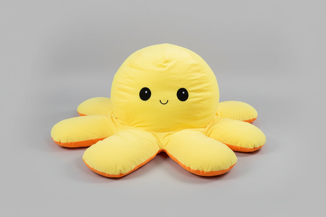 Yellow and orange reversible octopus plush toy with happy face on a light grey background.